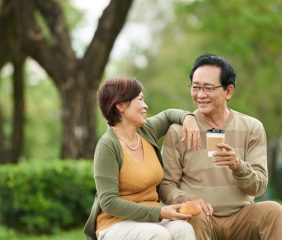 Senior smiling Vietnamese couple having coffee and buns in the park